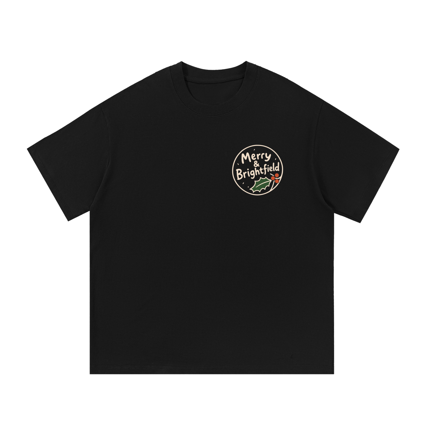 Mockup of a black cotton T-shirt with a small round chest badge reading 'Merry & Brightfield' beside a holly leaf