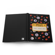 Black hardcover journal laid flat, back cover with barcode beside front cover with 'HELLO MY NAME IS' 'your name here' tag