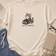 Garment-dyed unisex t-shirt featuring a cartoon cat in an EMT uniform — a 'Purr-amedic' pun tee for EMTs and paramedics.