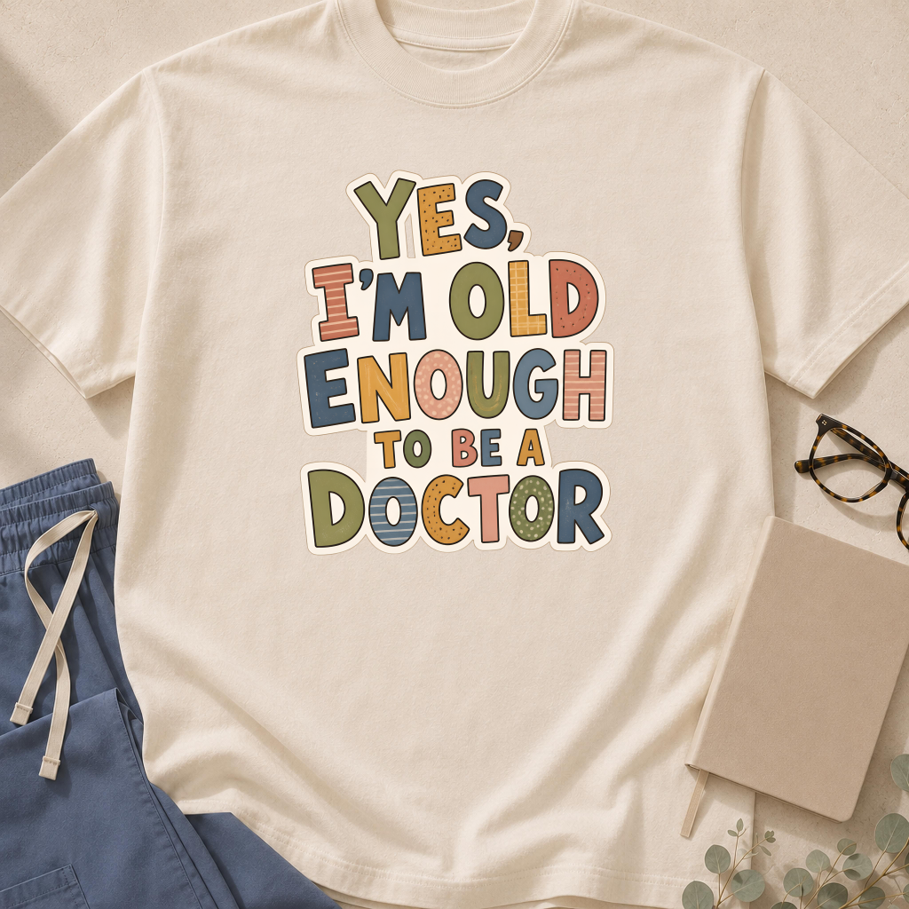 Garment-dyed unisex t-shirt in Bay printed with 'Yes, I'm Old Enough to Be a Doctor' — general medicine humor tee for young physicians.