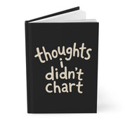 Mockup of a black hardcover journal, slightly open, with cream lettering reading 'thoughts i didn't chart'