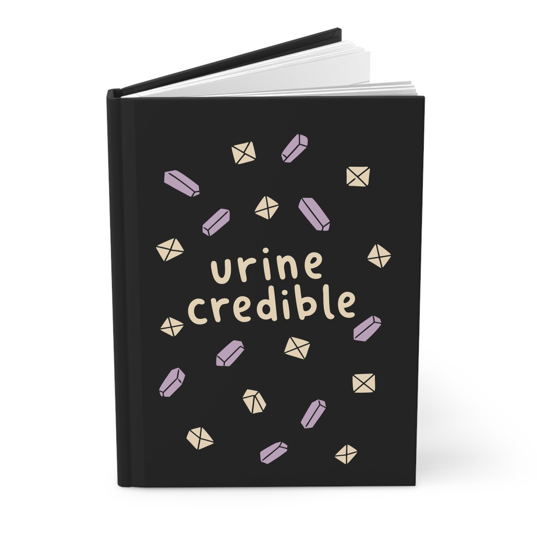 Black hardcover journal slightly open, cover reads 'urine credible' with lavender and cream crystals