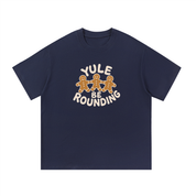 Mockup of a navy blue cotton T-shirt with three gingerbread men holding hands and the words 'Yule Be Rounding'