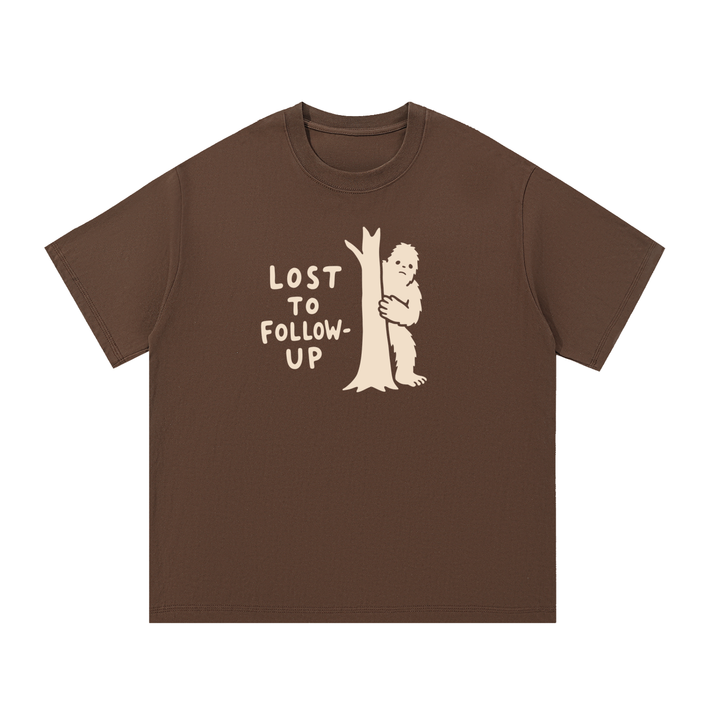 Mockup of coffee cotton T-shirt with a Big Foot hiding behind a tree with the words "Lost to follow-up".