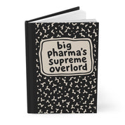 Angled view of black hardcover journal, cover reads 'big pharma's supreme overlord', pages visible