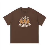 Mockup of a coffee brown cotton T-shirt with three gingerbread men holding hands and the words 'Yule Be Rounding'