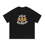Mockup of a black cotton T-shirt with three gingerbread men holding hands and the words 'Yule Be Rounding'