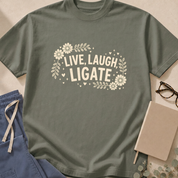 Garment-dyed unisex t-shirt printed with "Live Laugh Ligate" — surgery humor tee for surgeons and OR nurses.