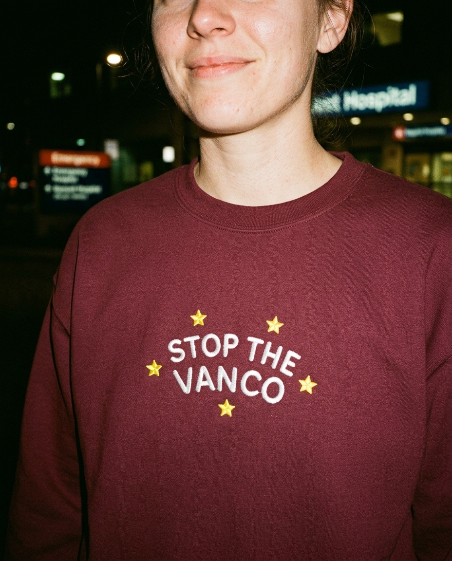 Model wearing the maroon embroidered 'Stop the Vanco' sweatshirt, close-up editorial flash photo outside a hospital at night.