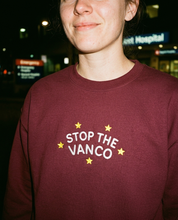 Model wearing the maroon embroidered 'Stop the Vanco' sweatshirt, close-up editorial flash photo outside a hospital at night.