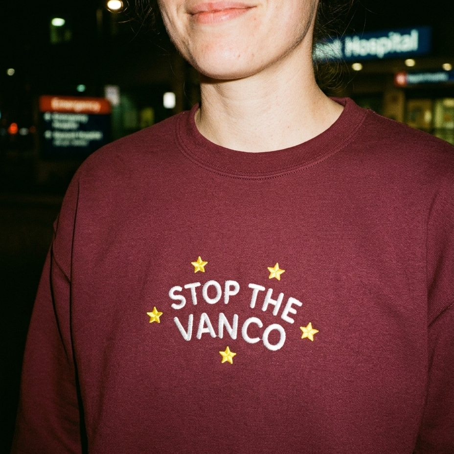 Model wearing the maroon embroidered 'Stop the Vanco' sweatshirt, close-up editorial flash photo outside a hospital at night.
