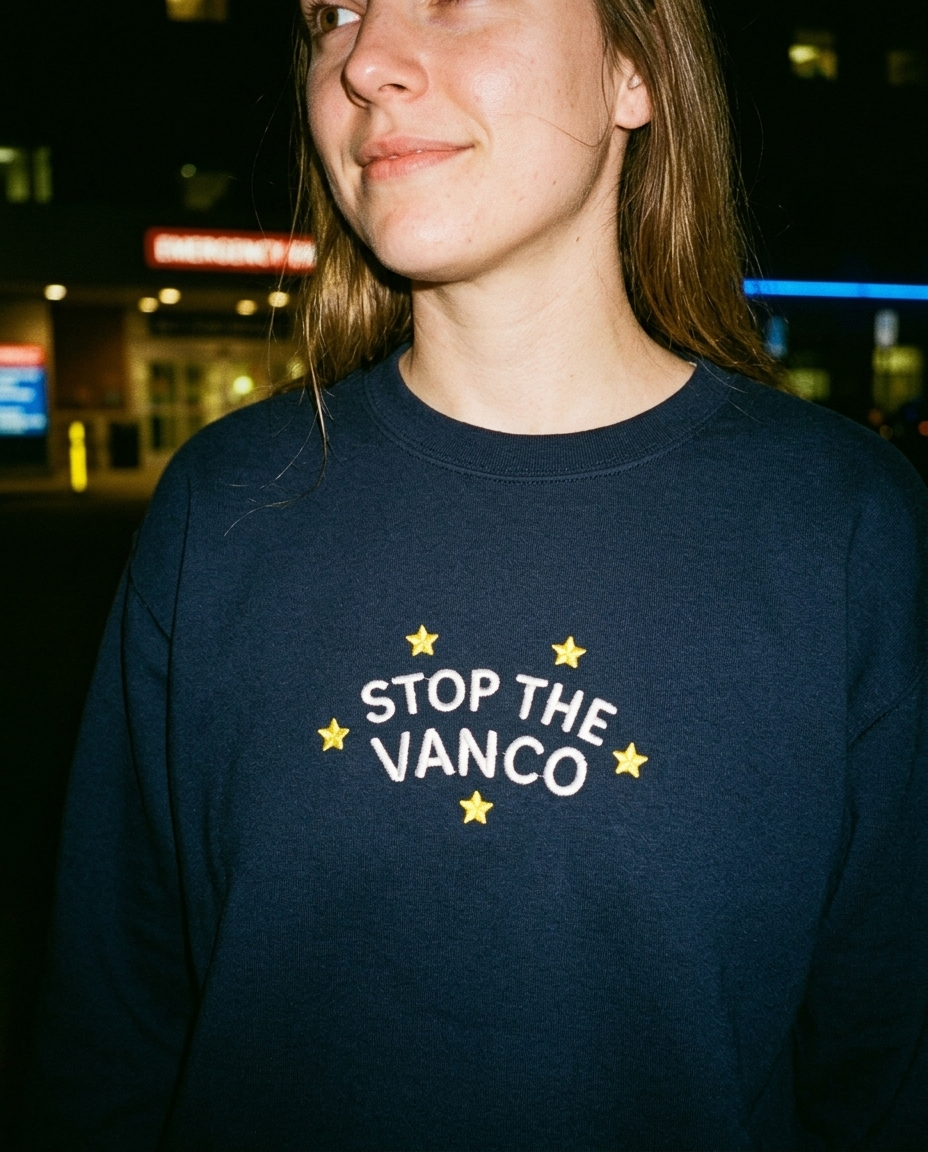 Model wearing the navy embroidered 'Stop the Vanco' sweatshirt, close-up editorial flash photo outside a hospital at night.