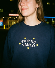 Model wearing the navy embroidered 'Stop the Vanco' sweatshirt, close-up editorial flash photo outside a hospital at night.