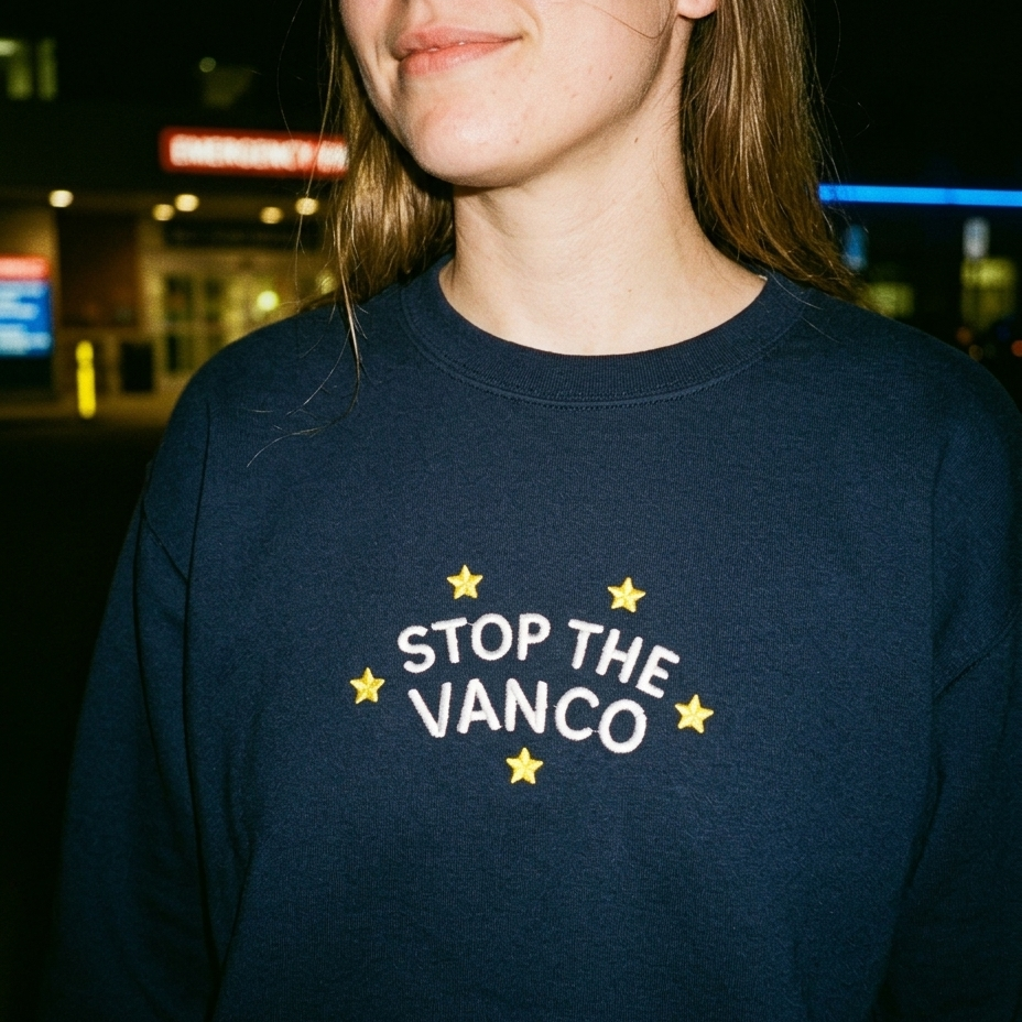 Model wearing the navy embroidered 'Stop the Vanco' sweatshirt, close-up editorial flash photo outside a hospital at night.