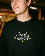 Model wearing the black embroidered 'Stop the Vanco' sweatshirt, close-up editorial flash photo outside a hospital at night.