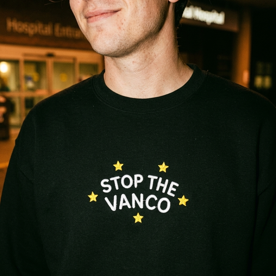 Model wearing the black embroidered 'Stop the Vanco' sweatshirt, close-up editorial flash photo outside a hospital at night.