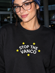 Model wearing the black embroidered 'Stop the Vanco' sweatshirt, daytime editorial flash photo outside a hospital.