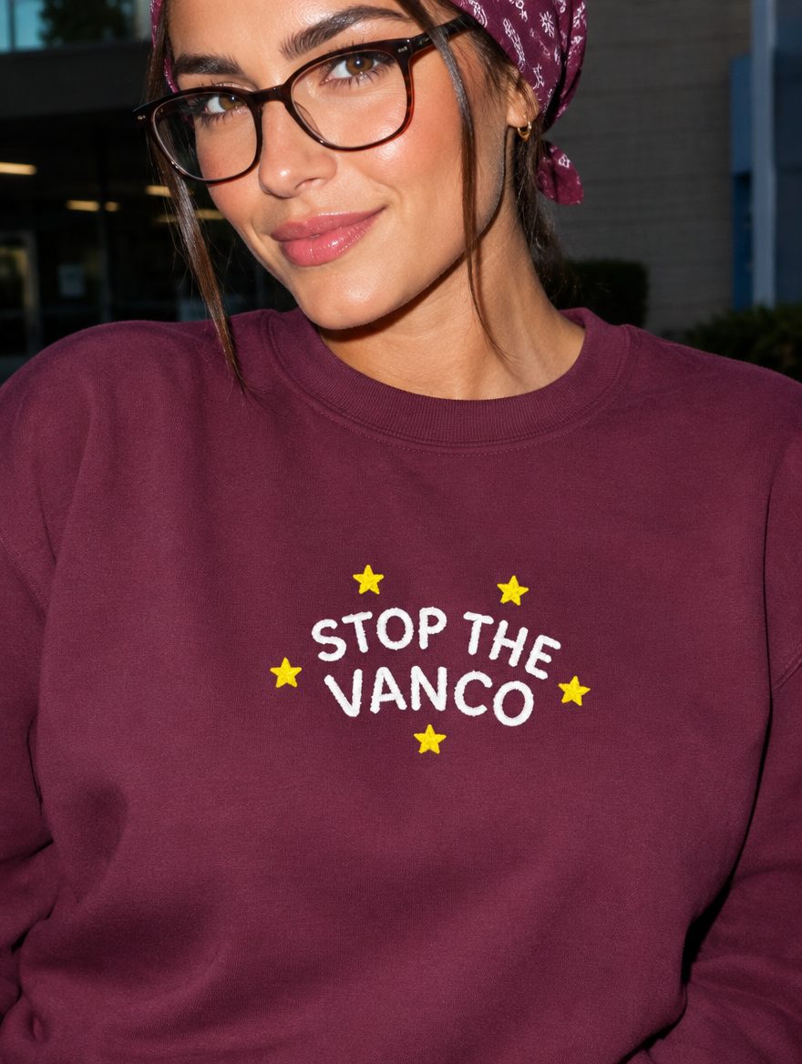 Model wearing the maroon embroidered 'Stop the Vanco' sweatshirt, daytime editorial flash photo outside a hospital.