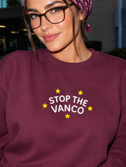 Model wearing the maroon embroidered 'Stop the Vanco' sweatshirt, daytime editorial flash photo outside a hospital.
