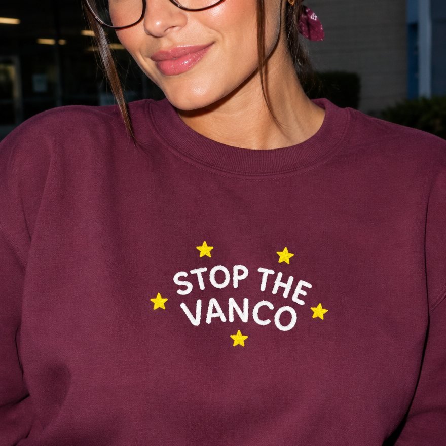 Model wearing the maroon embroidered 'Stop the Vanco' sweatshirt, daytime editorial flash photo outside a hospital.