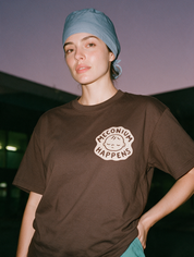 Woman photographed with flash at night, wearing a brown cotton T-shirt with small patch of a sleeping newborn face with the words 'Meconium Happens'.
