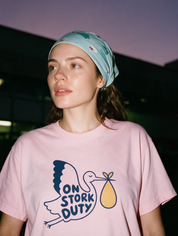 Woman photographed with flash at night, wearing a pink cotton T-shirt with stork carrying a bundle with the words 'On Stork Duty'.