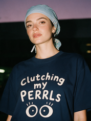 Woman photographed with flash at night, wearing a navy cotton T-shirt with two wide round eyes under the words 'Clutching my PERRLs'.