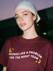 Woman photographed at night wearing a wine red cotton T-shirt with 'Sounds Like a Problem for the Night Team' design.