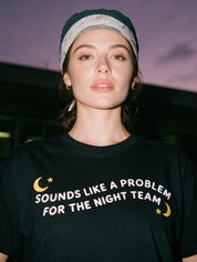 Woman photographed at night wearing a black cotton T-shirt with 'Sounds Like a Problem for the Night Team' design.