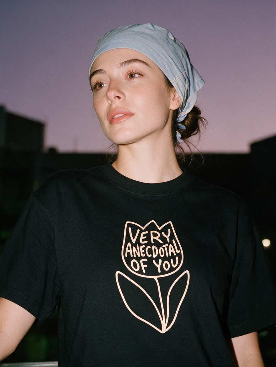 Woman photographed at night wearing a black cotton T-shirt with 'Very Anecdotal of You' design.