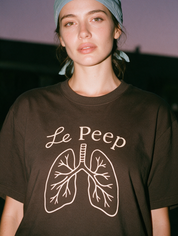 Woman photographed with flash at night, wearing a coffee brown cotton T-shirt with the 'Le Peep' design.