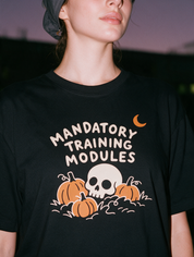 Woman photographed with flash at night, wearing a black cotton T-shirt with the 'Mandatory Training Modules' design.