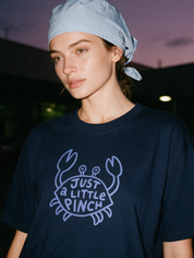 Woman photographed with flash at night, wearing a navy blue cotton T-shirt with the 'Just a Little Pinch' design.