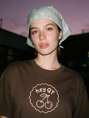 Woman photographed with flash at night, wearing a coffee brown cotton T-shirt with the 'Hey QT' design.