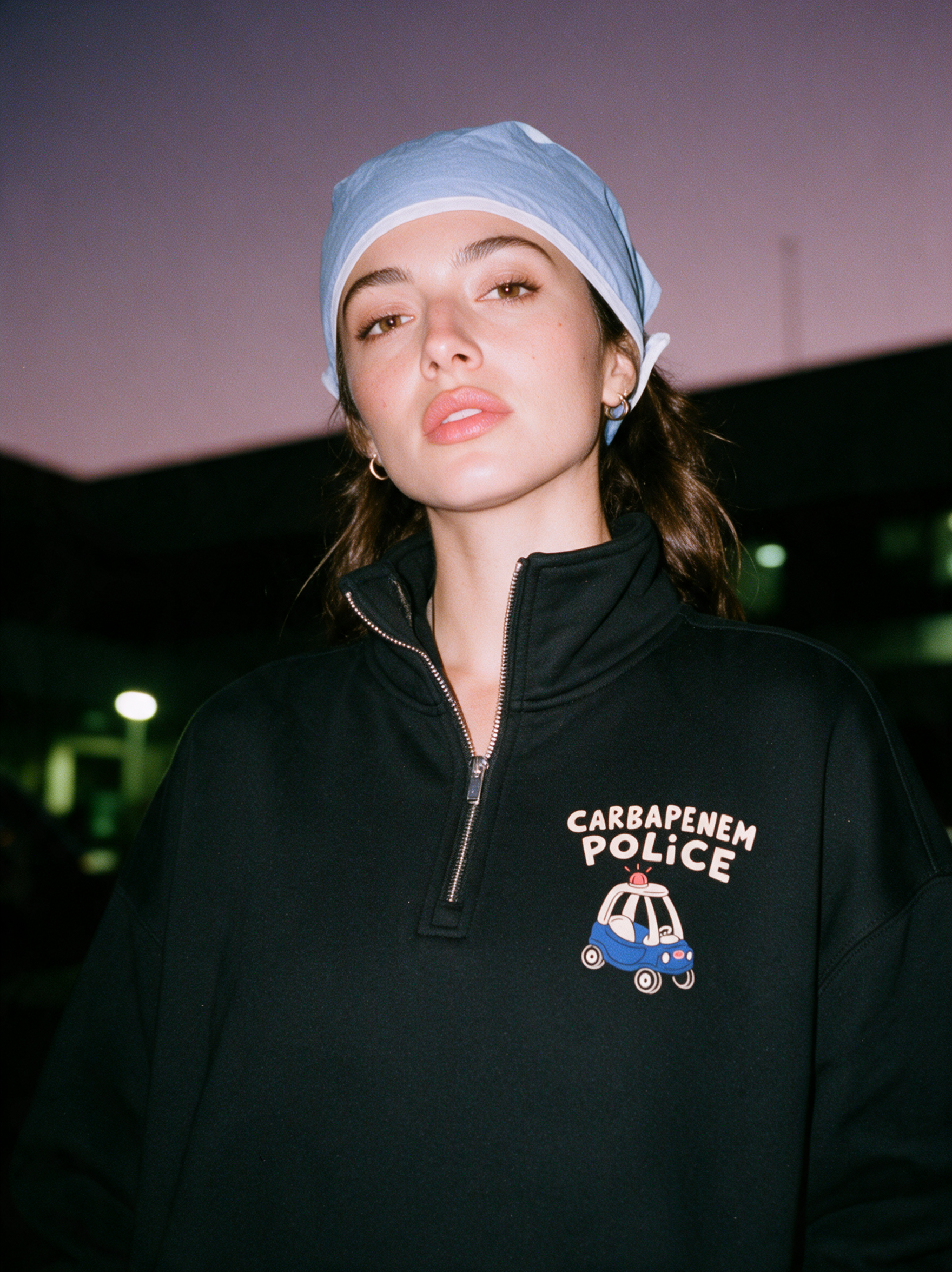 Physician wearing black 'Carbapenem Police' quarter-zip sweatshirt, night editorial photo