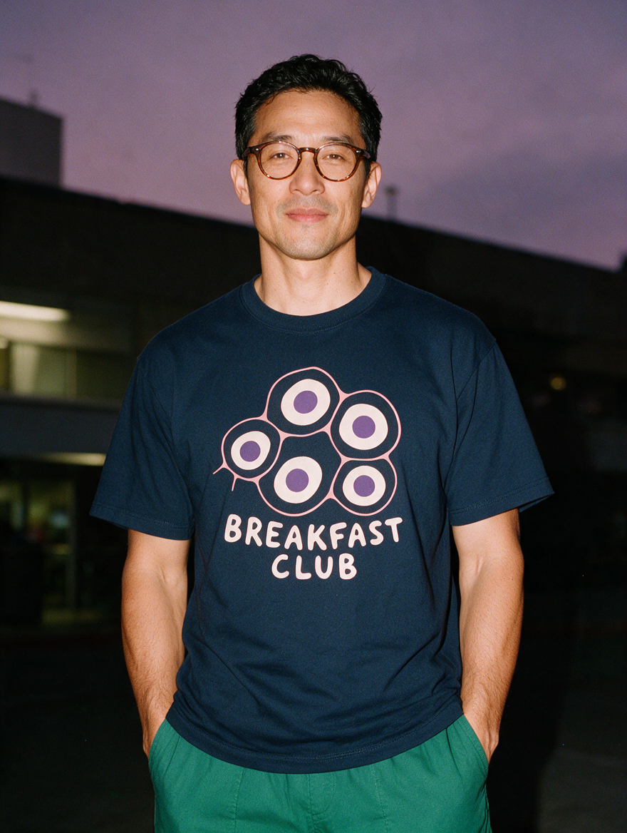 Man photographed with flash at night, wearing a navy blue cotton T-shirt with the Breakfast Club design.