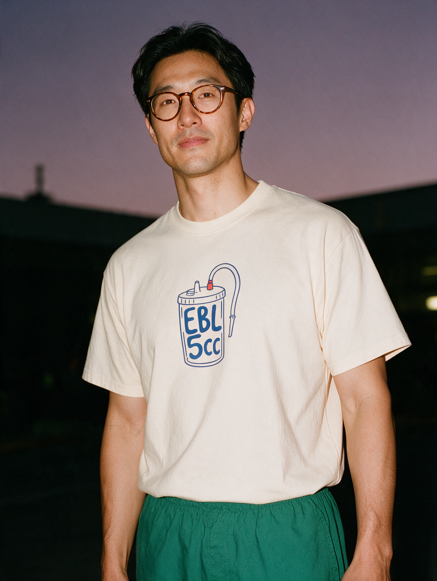 Man photographed with flash at night, wearing an apricot cotton T-shirt with the EBL 5cc design.