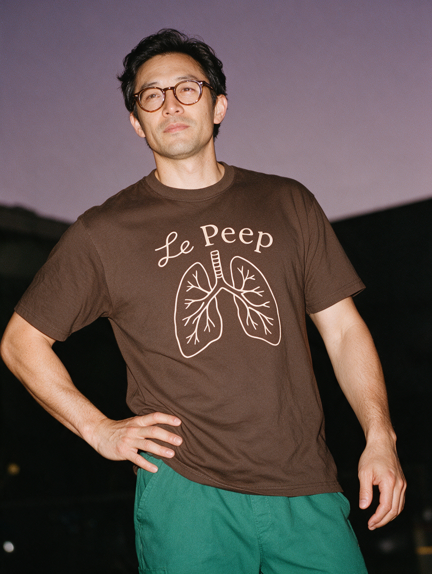 Man photographed with flash at night, wearing a coffee cotton T-shirt with the Le Peep design.