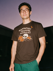 Man photographed with flash at night, wearing a coffee cotton T-shirt with the Mandatory Training Modules design.