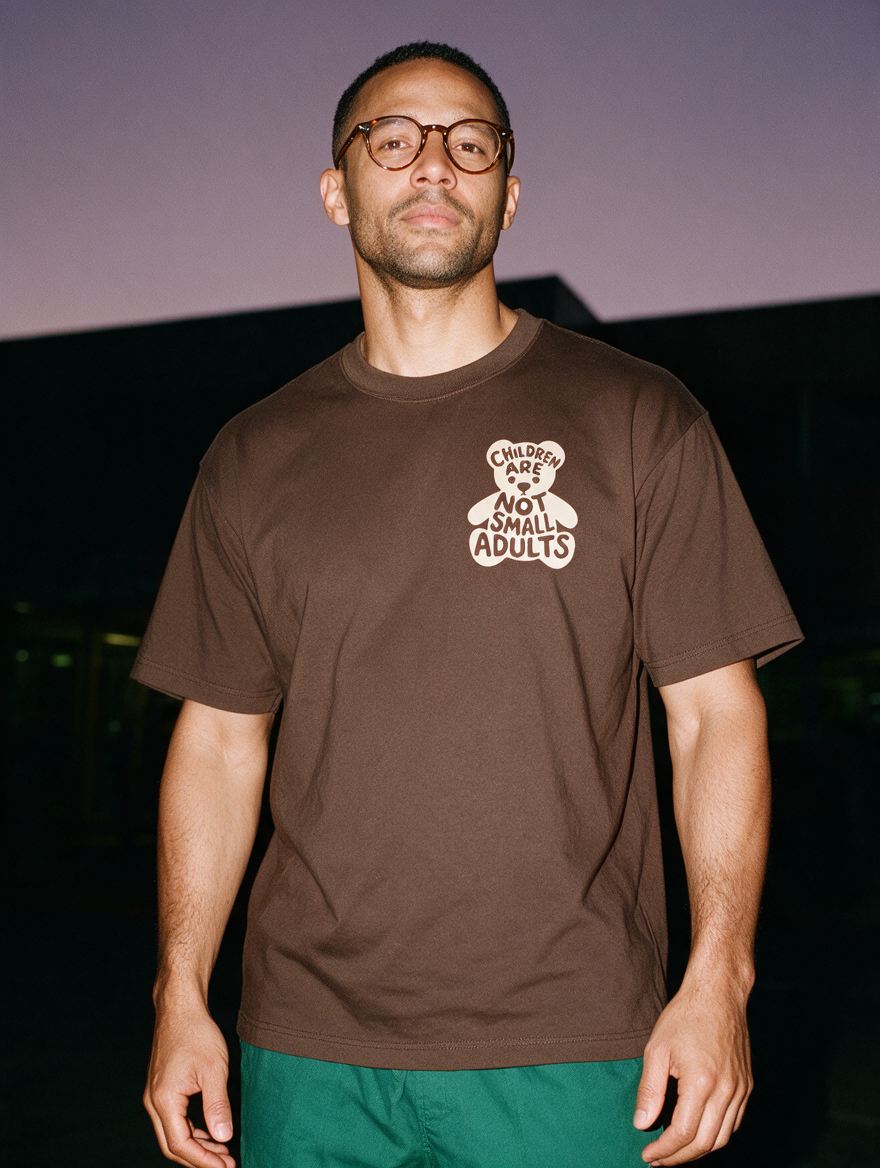 Man photographed with flash at night, wearing a coffee cotton T-shirt with the Children Are Not Small Adults design.