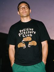 Man photographed with flash at night, wearing a black cotton T-shirt with the Positive Pressure Club design.
