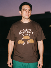 Man photographed with flash at night, wearing a coffee cotton T-shirt with the Positive Pressure Club design.