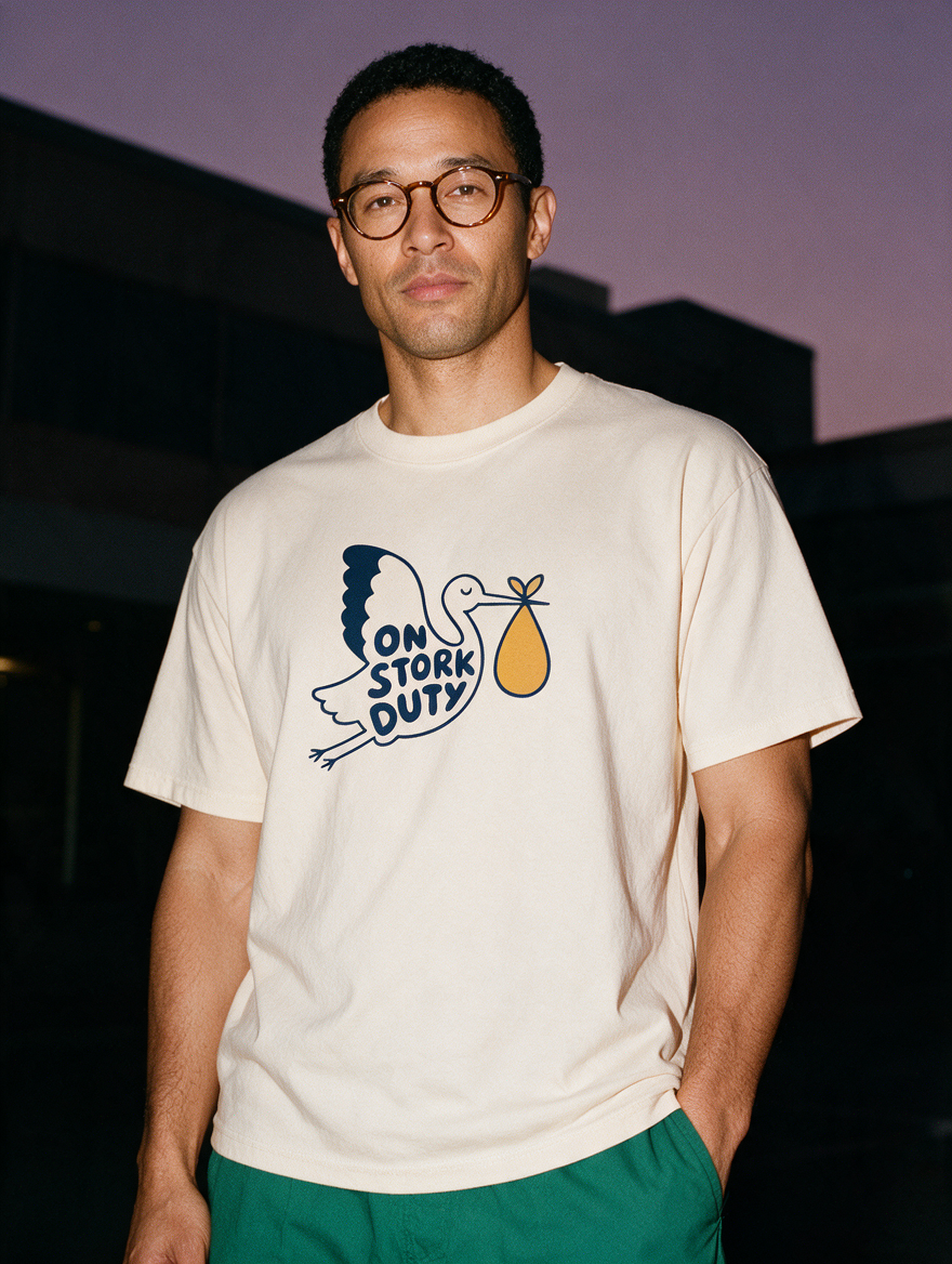 Man photographed with flash at night, wearing an apricot cotton T-shirt with the On Stork Duty design.