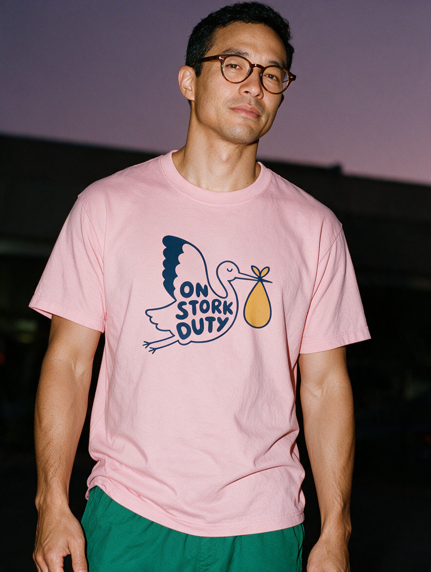 Man photographed with flash at night, wearing a pink cotton T-shirt with the On Stork Duty design.