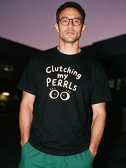 Man photographed with flash at night, wearing a black cotton T-shirt with the Clutching My PERRLs design.