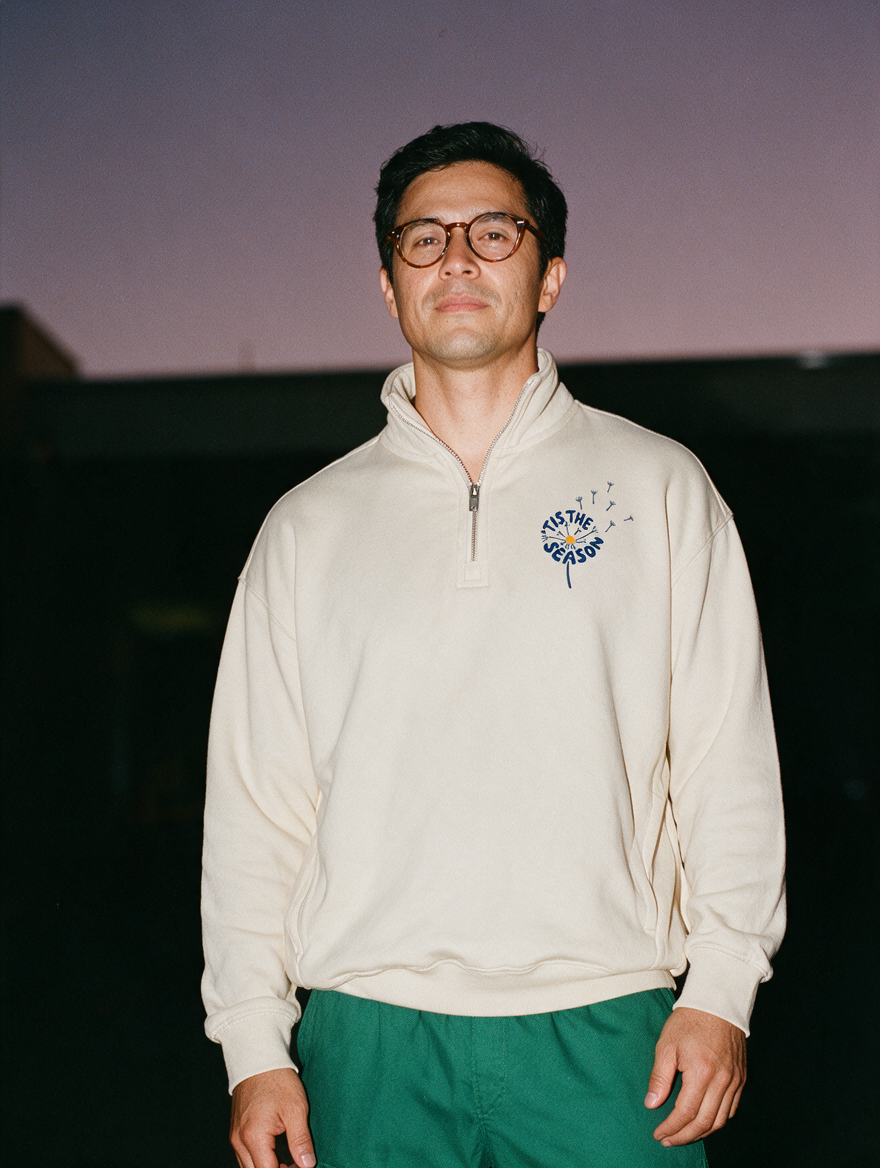 Man photographed with flash at night, wearing a light gray quarter-zip sweatshirt with the 'Tis the Season design.