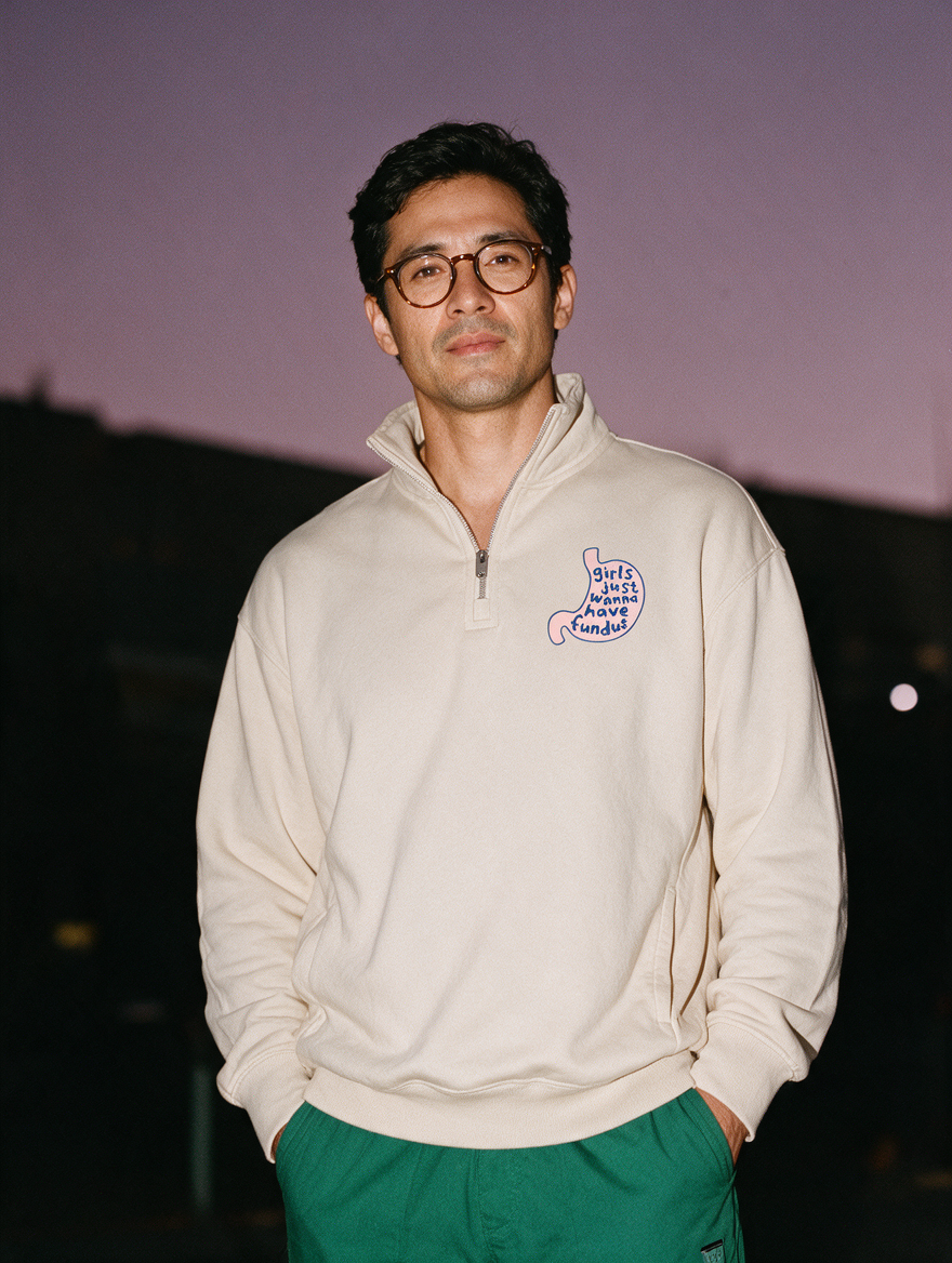 Man photographed with flash at night, wearing a light gray quarter-zip sweatshirt with the Girls Just Wanna Have Fundus design.