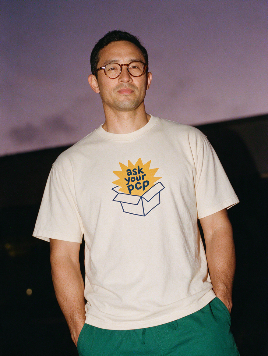 Man photographed with flash at night, wearing an apricot cotton T-shirt with the Ask Your PCP design.