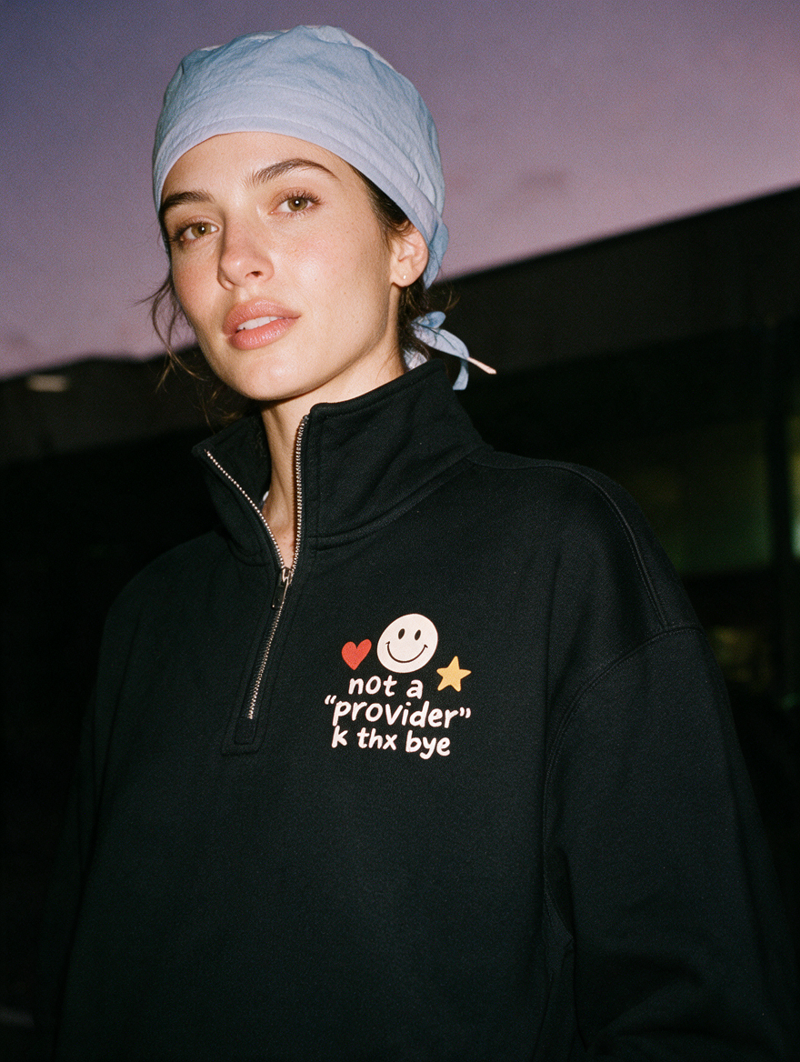 Woman photographed with flash at night, wearing a black quarter-zip sweatshirt with a smiley face, heart and star above 'not a "provider" k thx bye'.