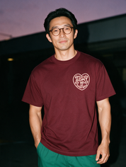 Man in round tortoiseshell glasses and green scrub pants, flash at night, wearing a wine red cotton T-shirt with a heart graphic 'Uptitrate GDMT for HFrEF as tolerated'